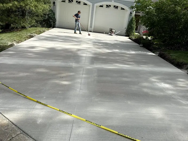 New broom-finished concrete driveway leading to a two-car garage, with the pour still taped off